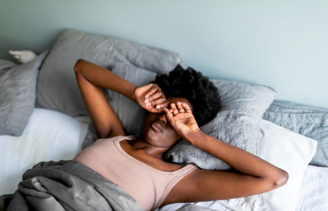 Kvinna med kvalsterallergi som ligger i sängen och kliar sig i ögonen.