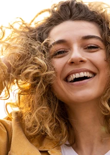 En kvinna står i solen och drar handen genom sitt lockiga hår. 