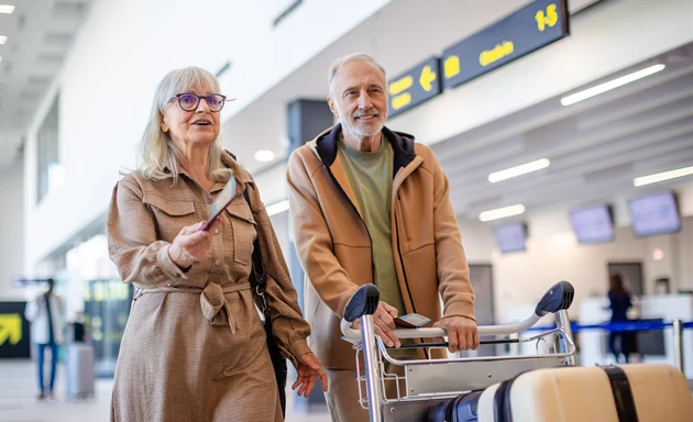 En äldre man och en kvinna med resväskor på flygplats.