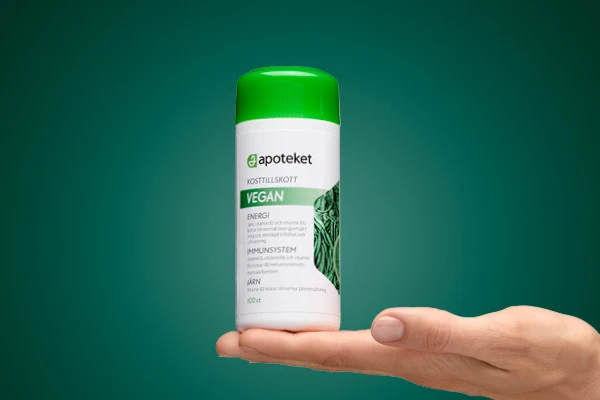 En hand visar upp kosttillskottet "VEGAN" från apoteket.