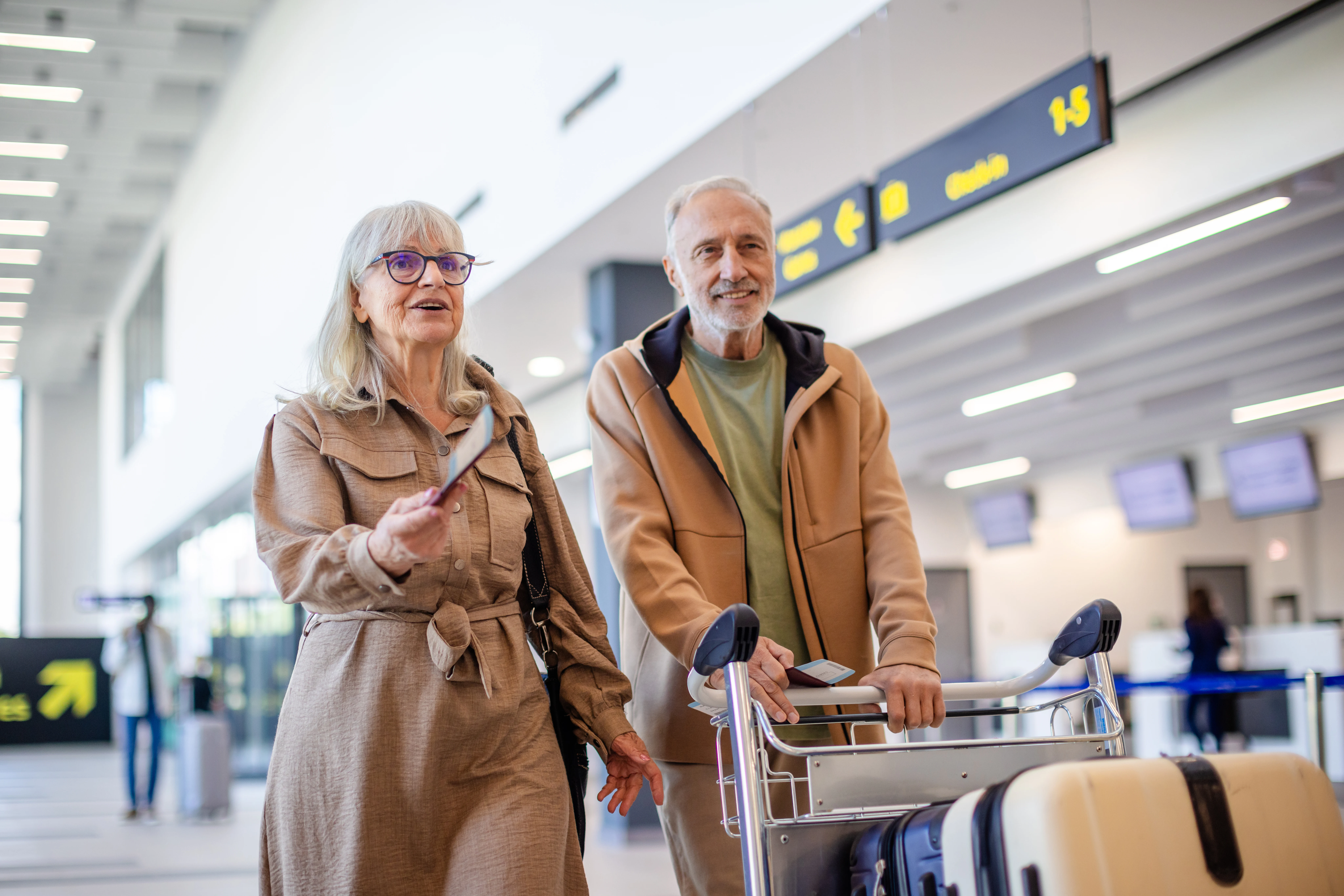 En äldre man och en kvinna med resväskor på flygplats.