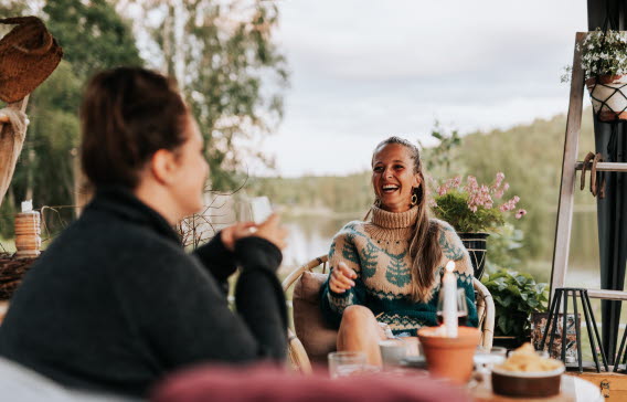 två kvinnor som sitter och pratar med varandra ute på en altan.