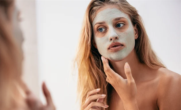 En kvinna i ett badrum smörjer försiktigt på en ansiktsmask med en subtil grön ton. 