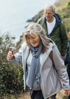 En grupp av seniorer promenerar på en stig vid ett hav. 