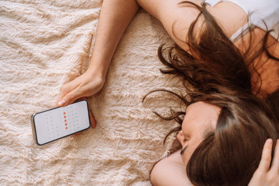 Tjej som kollar sin menscykel i en app. Herpes kan blomma upp under mensen.