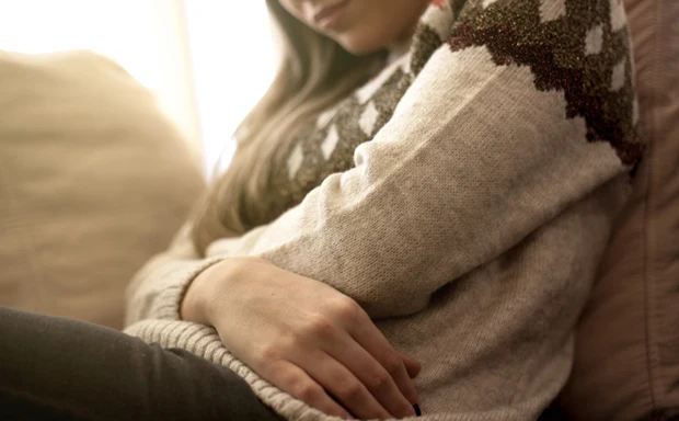 En kvinna sitter i en soffa och håller båda armarna om magen.