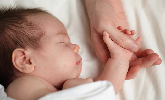 Liten sovande bebis med RS-virus som håller sin mammas hand.