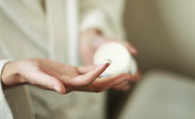 En person som tar hudkräm ur en förpackning.