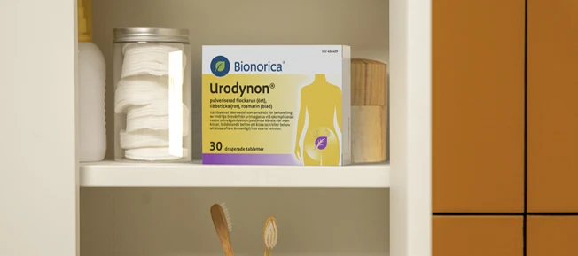 Ett badrumsskåp med en förpackning Urodynon, bomullsrondeller i glasburk och andra badrumsartiklar.