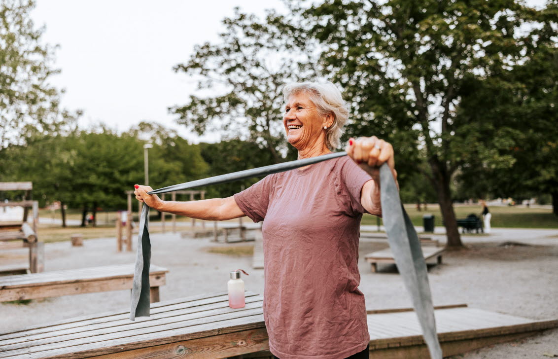 En äldre kvinna tränar med ett gummiband i en park.