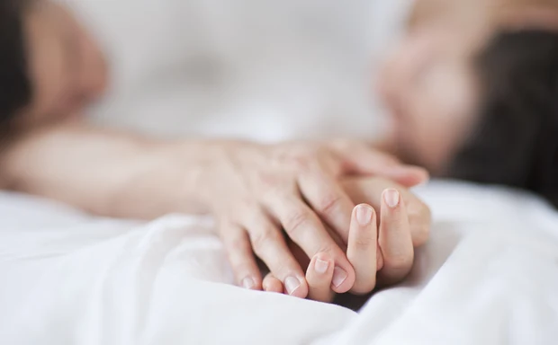 Två personer som håller händer i en säng. 