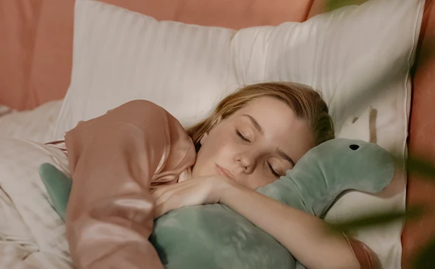 En kvinna sover i en säng och kramar om ett gossedjur. 