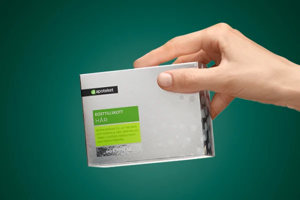 En hand visar upp kosttillskottet "HÅR" från apoteket.