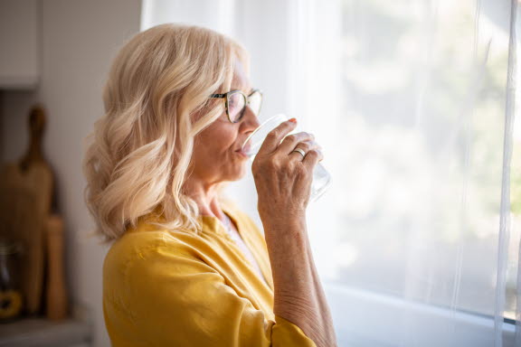 Kvinna som lindrar sin hesa röst med ett glas vatten.