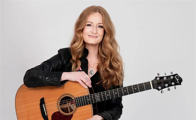 Anna Stadling sitter på en pall med en gitarr. 