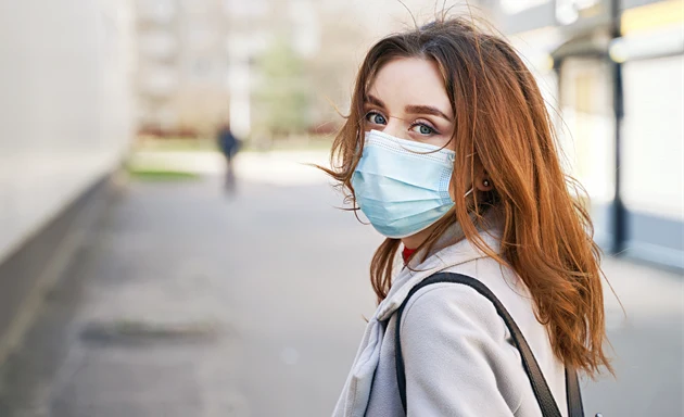 En kvinna med munskydd som står på en gata.