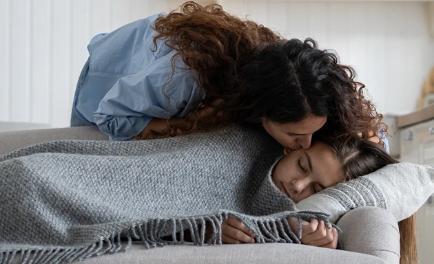 En mamma bäddar om sin sjuka dotter i en soffa. 