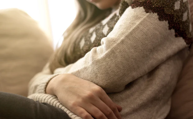 En kvinna sitter i en soffa och håller båda armarna om magen.