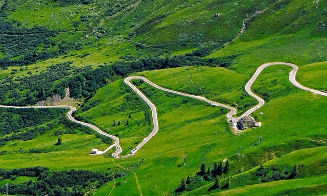 En slingrande väg genom gröna bergssluttningar med några byggnader och liftar.