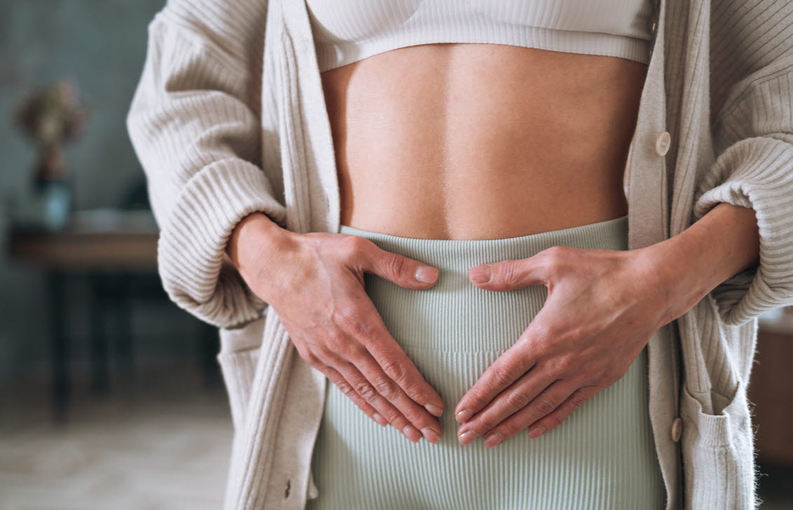 Kvinna med myom som håller sig på magen.