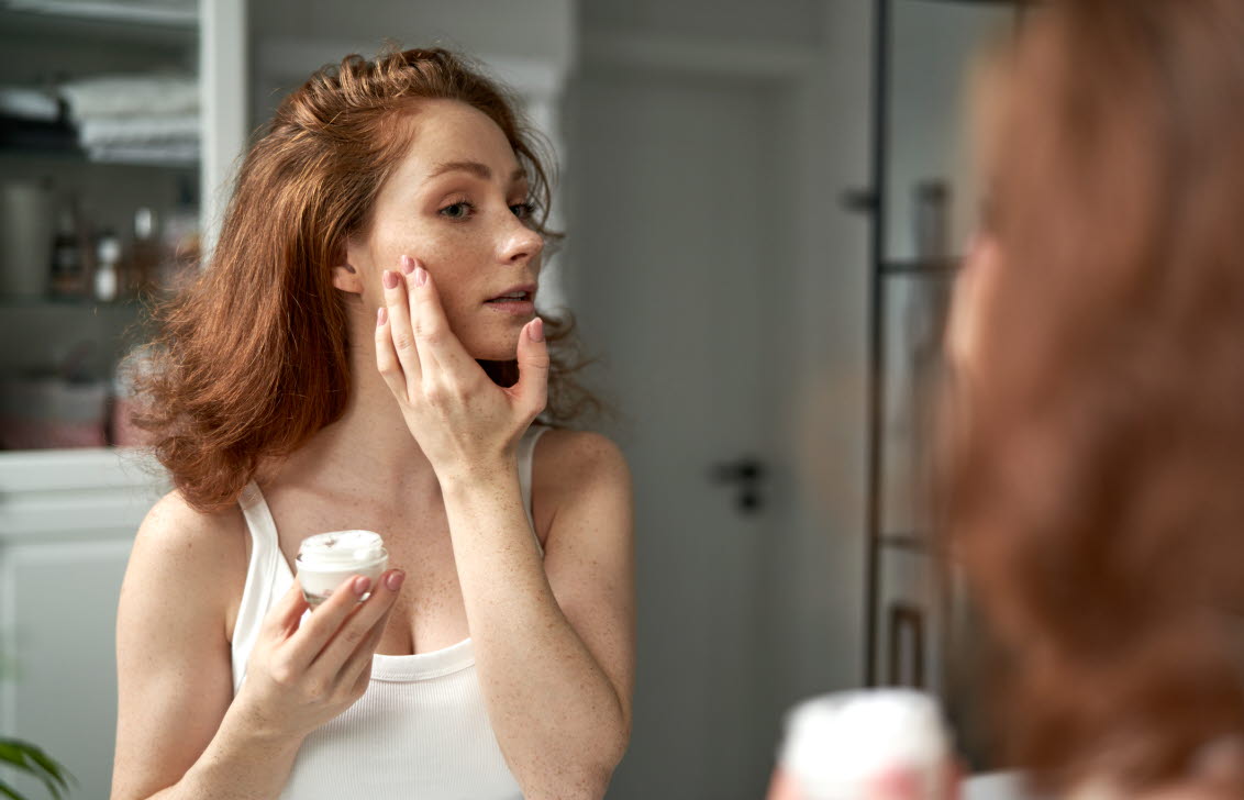 Kvinna med rosacea som applicerar ansiktskräm.