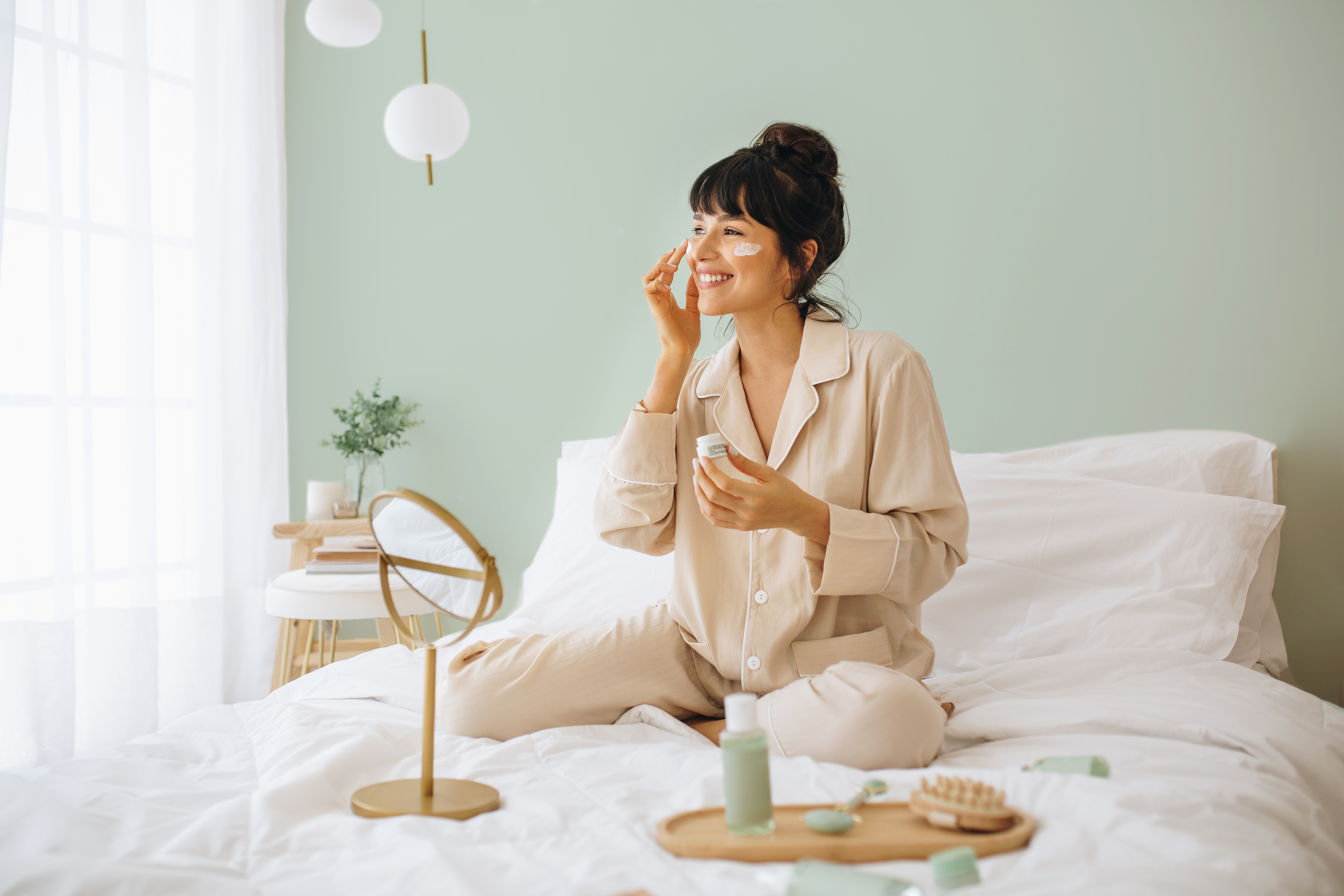 Tjej som sitter i sängen och applicerar en peptidkräm.