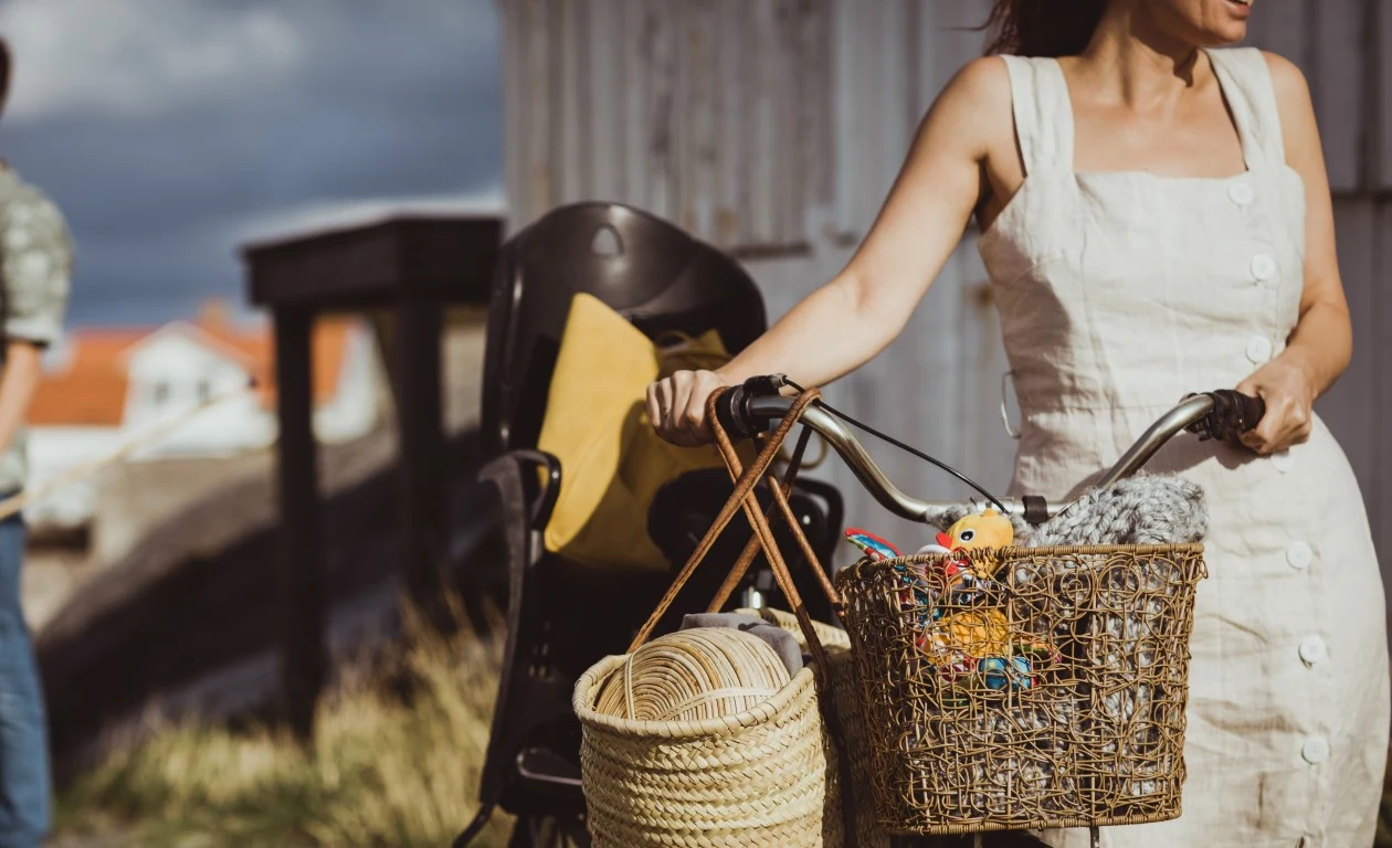 Kvinna i sommarklänning leder sin cykel längs en grusväg i skärgården.