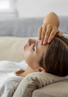 Ung kvinna med migrän som vilar i en soffa.