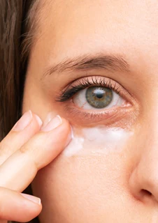 En kvinna applicerar hudvård under sina ögon.