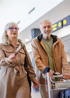 En äldre man och en kvinna med resväskor på flygplats.