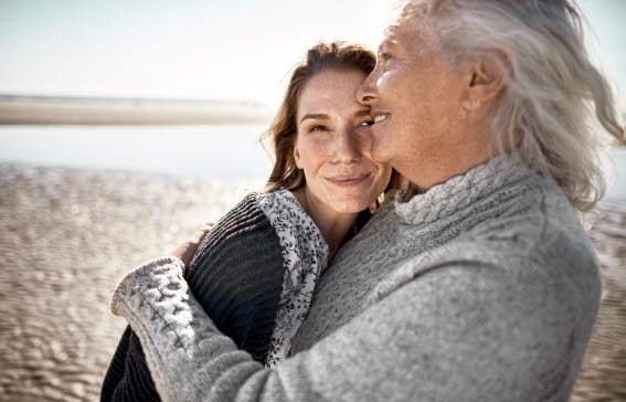 Kärleksfull äldre kvinna med sin vuxna dotter på stranden.
