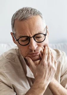 En man med tandvärk håller händerna över ena käken. 