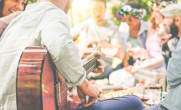 Personer som sitter runt ett bord och spelar gitarr på midsommar.