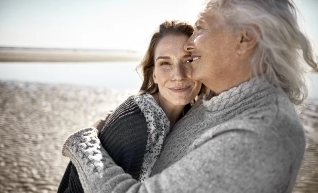 En äldre kvinna håller om sitt barnbarn på stranden.