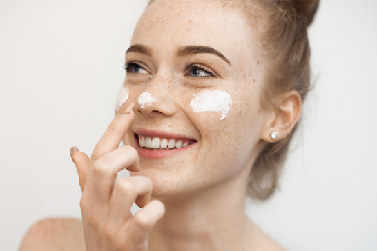 Tjej med känslig hud som applicerar ansiktskräm.