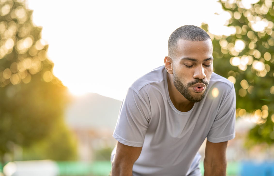 En ung man böjer sig fram och andas djupt efter ett träningspass utomhus.
