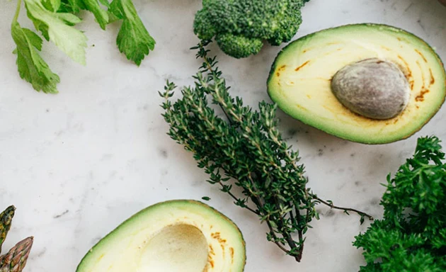 Avocado, broccoli och andra grönsaker ligger på ett bord.