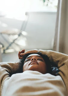 En kvinna ligger i en säng med händerna ovanför huvudet. 