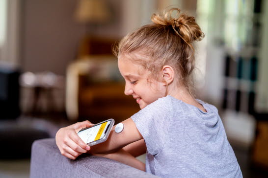 En flicka läser av sin CGM-sensor med en mobiltelefon.