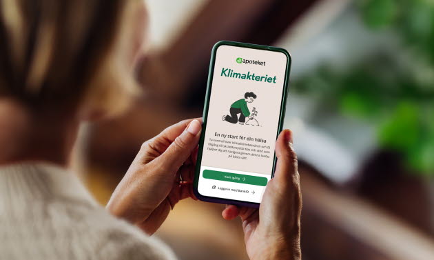En kvinna håller i en mobil och har öppnat Apotekets Klimakterieapp.