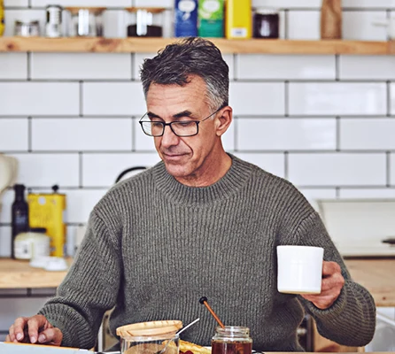 En man sitter i köket, äter frukost och dricker kaffe.