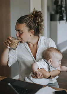 Stressad mamma som dricker kaffe, jobbar och tar hand om sin bebis.