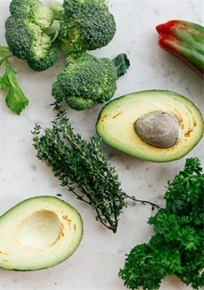 Avocado, broccoli och andra grönsaker ligger på ett bord.
