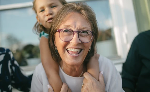 Glad medelålders kvinna som har sitt barnbarn på ryggen.