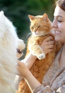 Kvinna som gosar med en hund och en katt.