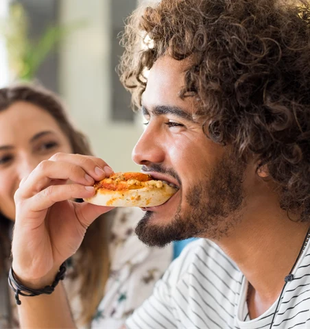 En man tar en tugga av en pizzabit.
