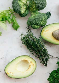 Avocado, broccoli och andra grönsaker ligger på ett bord.