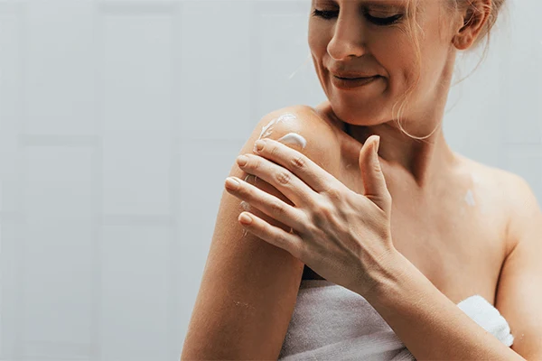 En kvinna smörjer in sin axel med återfuktande lotion. 