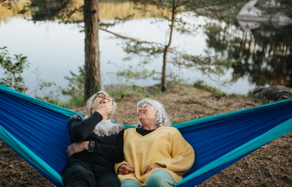 Två äldre kvinnor vilar i en hängmatta vid sjön.