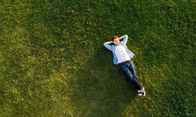 En man ligger på en stor gräsplätt.